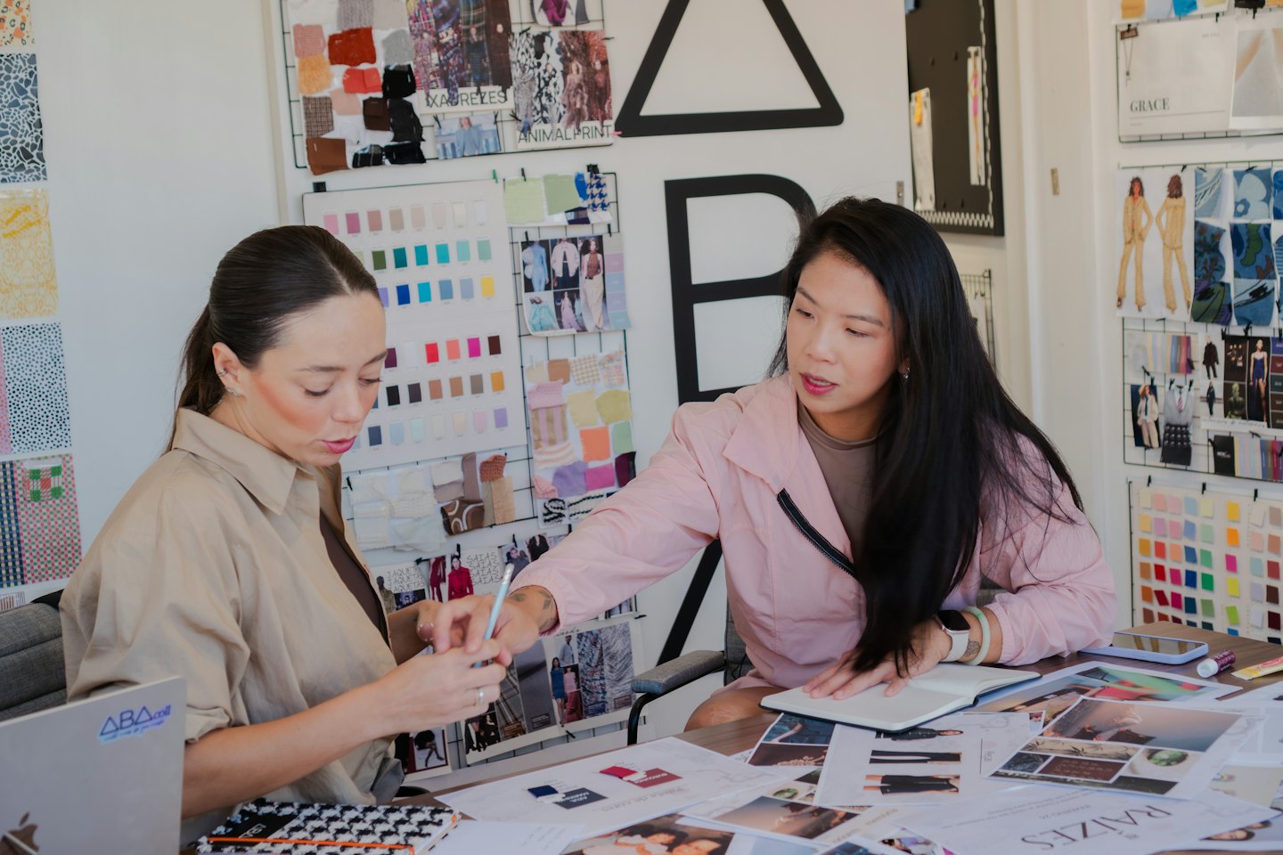 Due donne collaborano a disegni di moda con schizzi e campioni di tessuto.