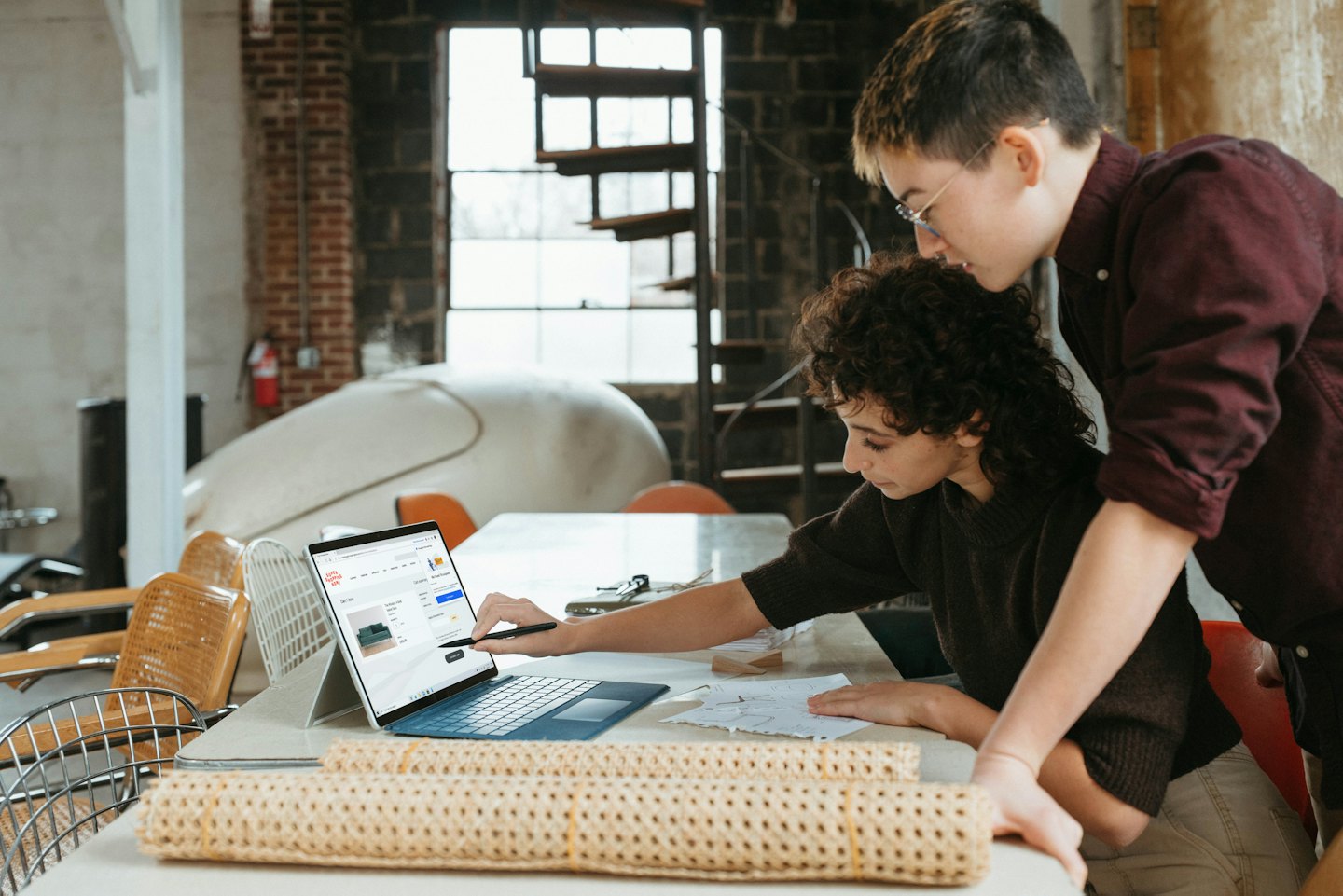 Due designer collaborano a un laptop con immagini di prodotti sullo schermo.