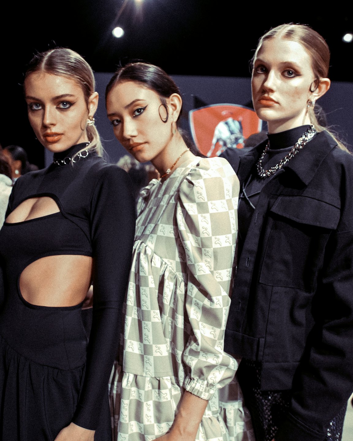 Tre modelle con outfit alla moda posano nel backstage di un evento.