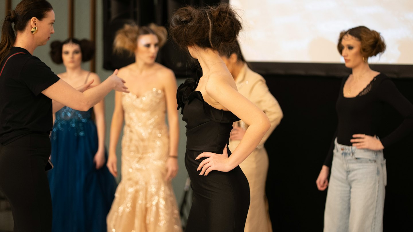 Una stilista gesticola mentre dirige le modelle in uno studio di moda.